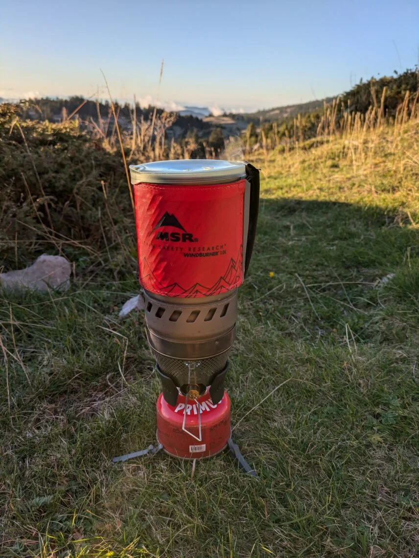 Réchaud MSR WindBurner monté sur sa cartouche de gaz, posé dans l'herbe en montagne