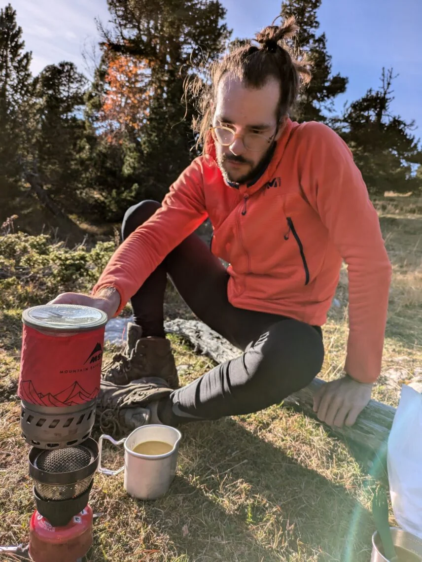 Randonneur soulevant le couvercle du pot MSR WindBurner à côté d'une tasse remplie