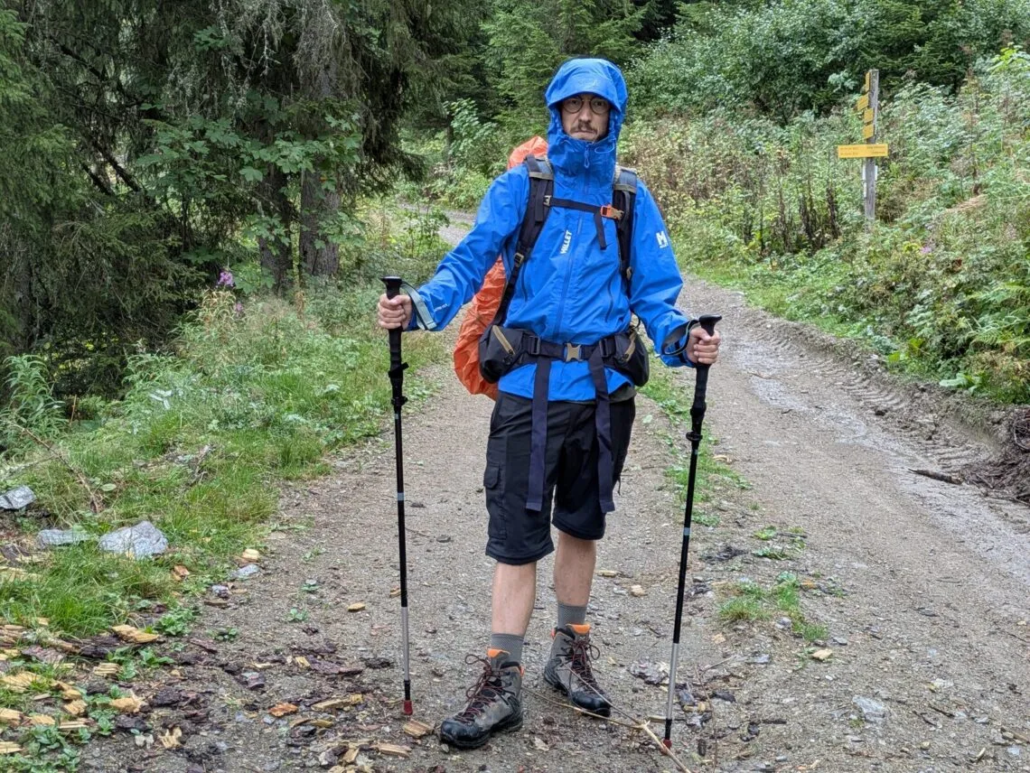Randonneur en veste Millet Kamet Light capuche fermée sous une averse en forêt