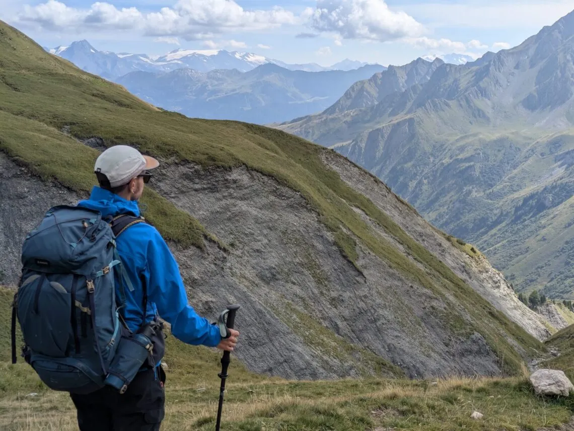Randonneur de dos en veste Millet Kamet Light devant un panorama de sommets alpins